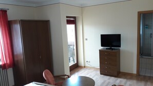 A room with a wooden wardrobe, a television on a cabinet, a chair, and a window with blinds. - Pension Zum Schwan (Muhr am See)