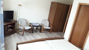 A hotel room with a bed, two striped armchairs, a small table with a magazine, a TV on a stand, and a wardrobe. - Pension Zum Schwan (Muhr am See)