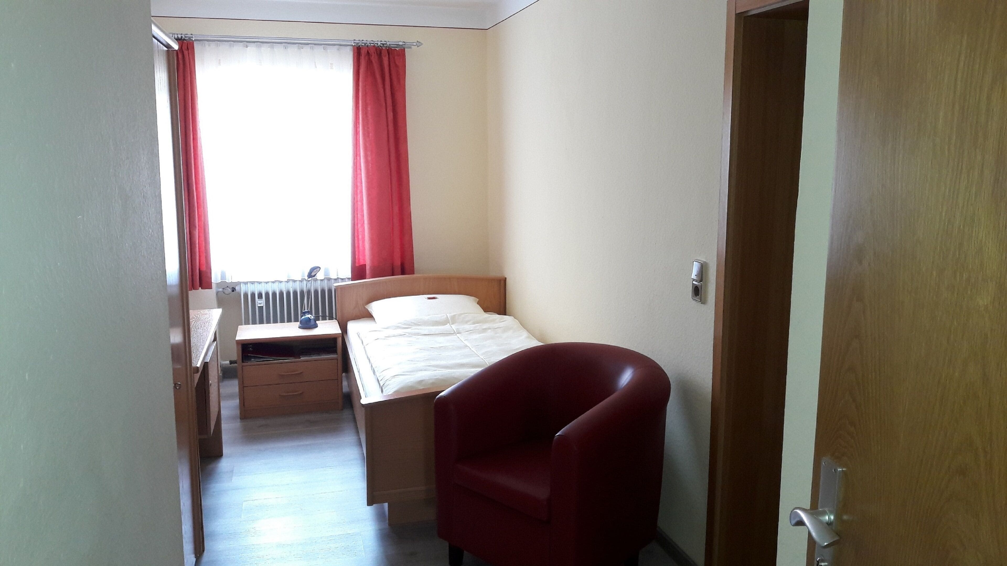 A small, simple room with a bed, a desk, and a chair.
