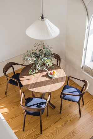 A round wooden dining table with two chairs, a hanging light fixture, and a potted plant. - Flattered to be in Porto Sea View Apartment A (Oporto)