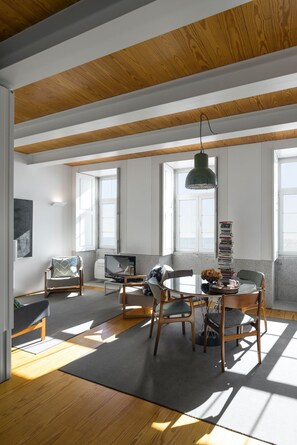 Un salon moderne avec un plafond en bois, une table de salle à manger ronde entourée de chaises, un canapé et un téléviseur.