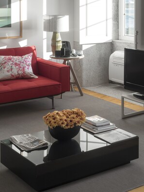A modern living room with a red sofa, a black coffee table with a vase of flowers, a television, and a small side table with a lamp.