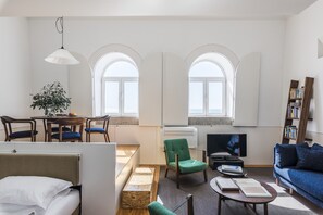A modern living room with a sofa, a dining table with chairs, a TV, and a bookshelf.
