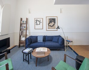 A modern living room with a blue sofa, a wooden bookshelf, a round coffee table, and a TV. - Flattered to be in Porto Sea View Apartment A (Oporto)
