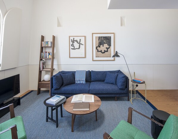 A modern living room with a blue sofa, a wooden bookshelf, a round coffee table, and a TV. - Flattered to be in Porto Sea View Apartment A (Oporto)