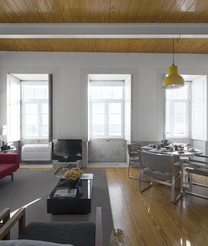 Un salon moderne doté d’un téléviseur, d’un canapé rouge, d’un coin repas avec une table et des chaises, et de grandes fenêtres offrant une vue dégagée.