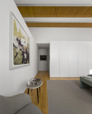 A modern living room with a grey sofa, a small round table, and a grey rug. There is a large framed picture on the wall and a white wardrobe in the background.