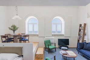 A modern living room with a dining area, a green armchair, a TV, and a bookshelf. - Flattered to be in Porto Sea View Apartment A (Oporto)