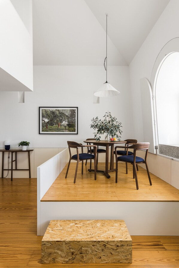 A modern dining area with a wooden table, chairs, and a hanging light fixture. - Flattered to be in Porto Sea View Apartment A (Oporto)