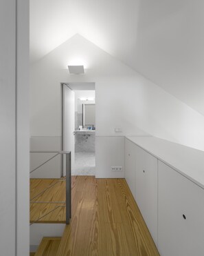 Un escalier moderne et épuré menant à une salle de bain dotée d’un plancher en bois et de murs blancs.