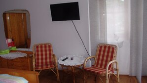 A room with a television mounted on the wall, two wicker chairs, a small round table with a lace tablecloth, and a wooden wardrobe. - Eulenberghof Kraus (Altenkunstadt)