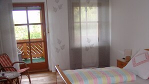 A room with a wooden bed, a chair, a table, and a view through a glass door to an outdoor area. - Eulenberghof Kraus (Altenkunstadt)