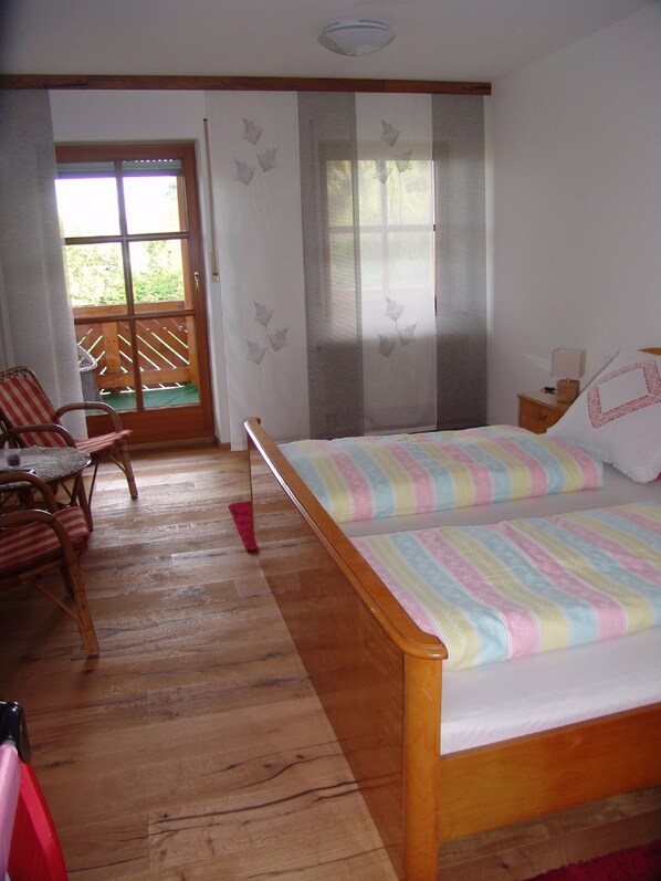 Une pièce avec un lit en bois, une chaise, une table et une vue sur un espace extérieur, accessible par une porte vitrée.