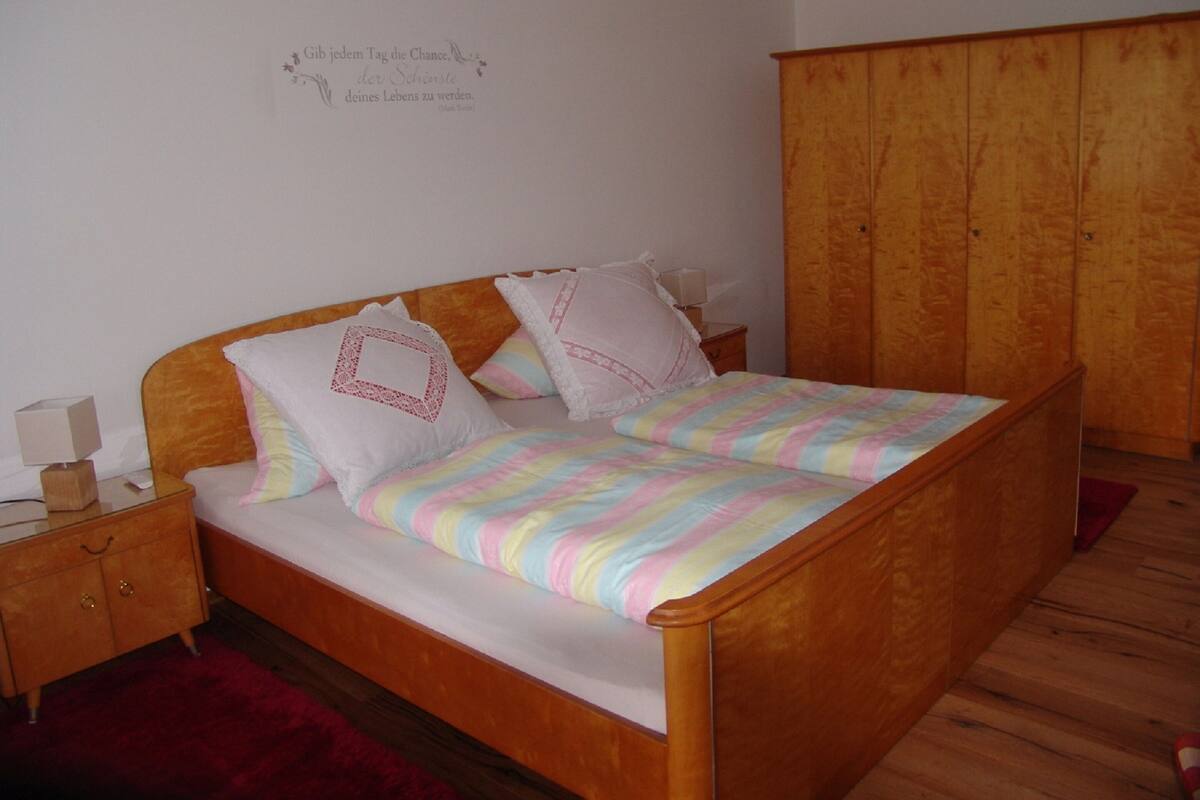 A bed with a wooden headboard, two bedside tables, a red rug, and a wooden wardrobe.