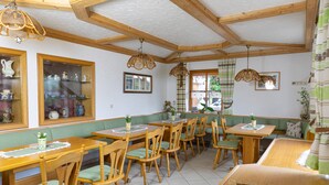 A restaurant with wooden tables and chairs, green cushioned seating, and hanging light fixtures. - Eulenberghof Kraus (Altenkunstadt)