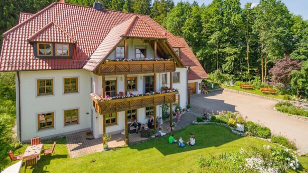 A two-story building with a red-tiled roof, wooden balconies, and a garden area with benches and flowers. - Eulenberghof Kraus (Altenkunstadt)