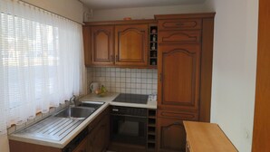 Uma cozinha com armários de madeira, pia, lava-louças e janela com cortina fina.