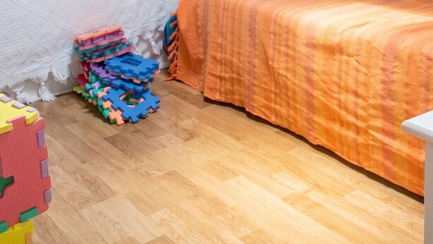 Une chambre avec un plafond en bois, un lit recouvert d’une couverture orange, une tête de lit blanche et, sur le sol, des tapis de sol en mousse colorés et modulaires.