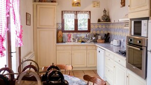 Une cuisine avec des meubles blancs, un four à micro-ondes, un four, un évier et un coin repas avec des chaises.