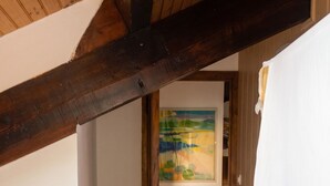 Une pièce avec des poutres en bois, un radiateur blanc, une porte donnant sur une autre pièce et des tapis en mousse colorés sur le sol.