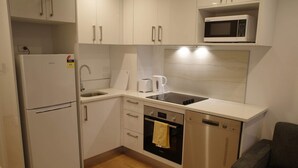 A compact kitchen with white cabinets, a built-in microwave, a refrigerator, a sink, a toaster, and a dishwasher.