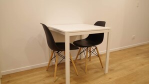 A white table with two black chairs in a room with wooden flooring and white walls.