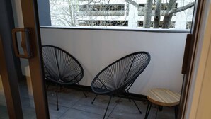 A balcony with two black wire-framed chairs and a small wooden stool.
