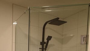 A glass-enclosed shower with a handheld showerhead and a wall-mounted faucet.