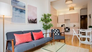 Una sala de estar moderna con un sofá gris, cojines rojos, una mesa de centro de vidrio y una zona de comedor con una mesa y sillas blancas.