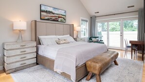 A bedroom with a large bed, a bench, a dresser, and a painting on the wall.
