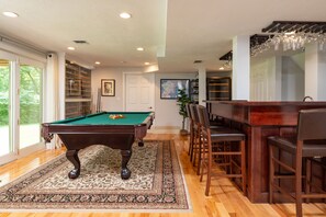 Enjoy a game of pool or relax with a drink at the bar, surrounded by a comfortable seating area and a large window with an outdoor view.