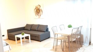 A living room with a sofa, a small table, and a dining area with chairs and a table. - Philips Apartment (Milan)