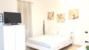 A bedroom with a bed, a TV on a cabinet, and wall-mounted artwork. - Philips Apartment (Milan)