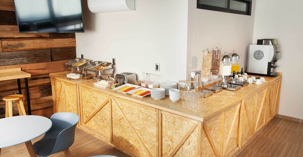 Una barra de desayuno con diversas opciones de alimentos, una máquina de café y asientos.