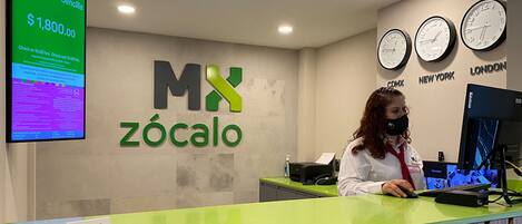 Un mostrador de recepción con una pantalla digital, un reloj y un cartel que dice 'MX zócalo'.