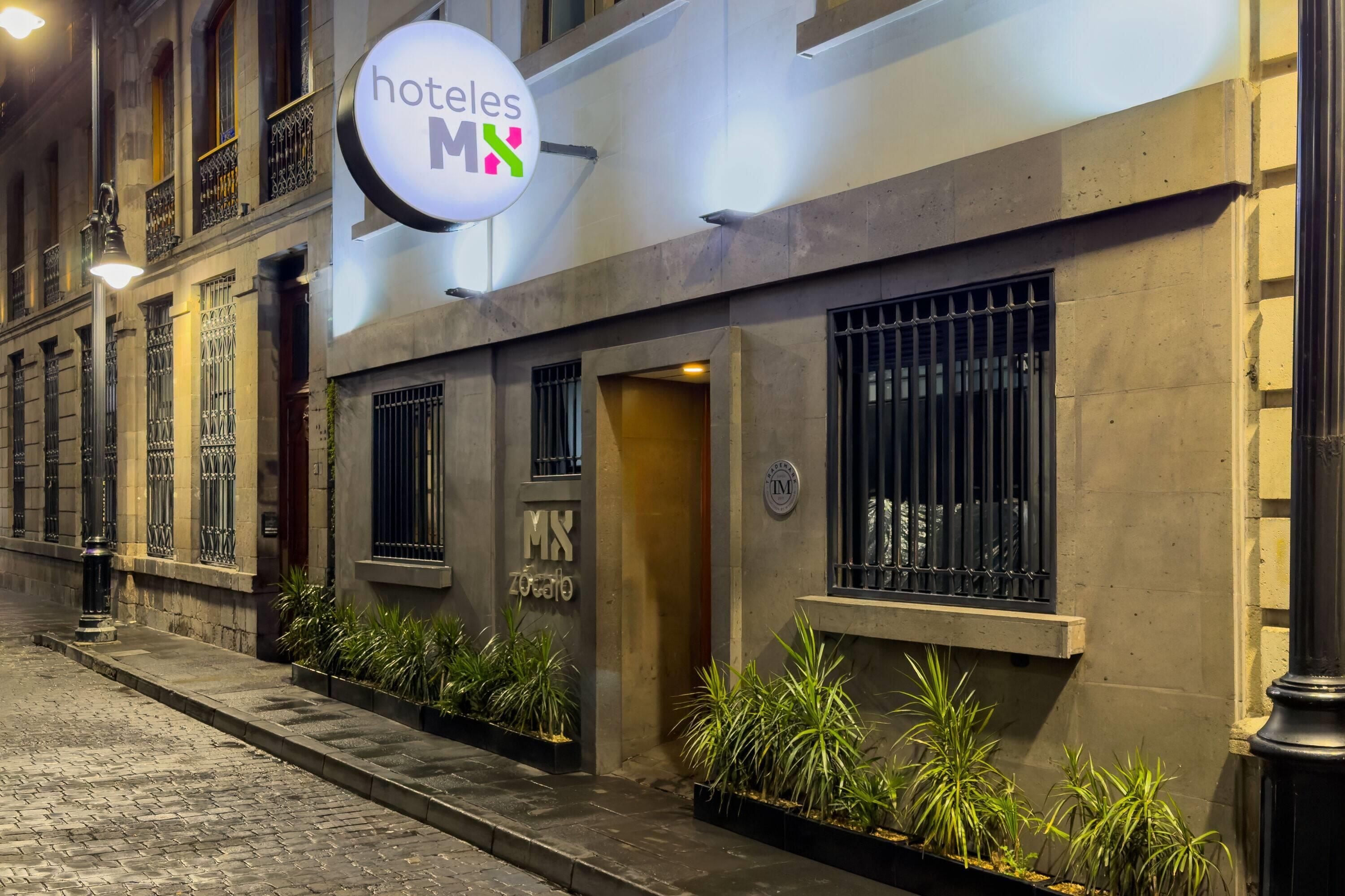 La façade d’un hôtel, avec une enseigne indiquant « hoteles MX » et un logo représentant une maison et un cœur.