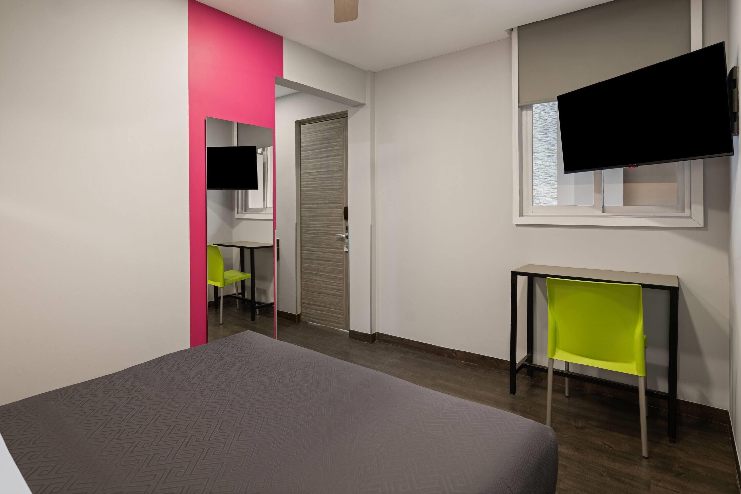 A room with a bed, a desk, a chair, a television, and a door.