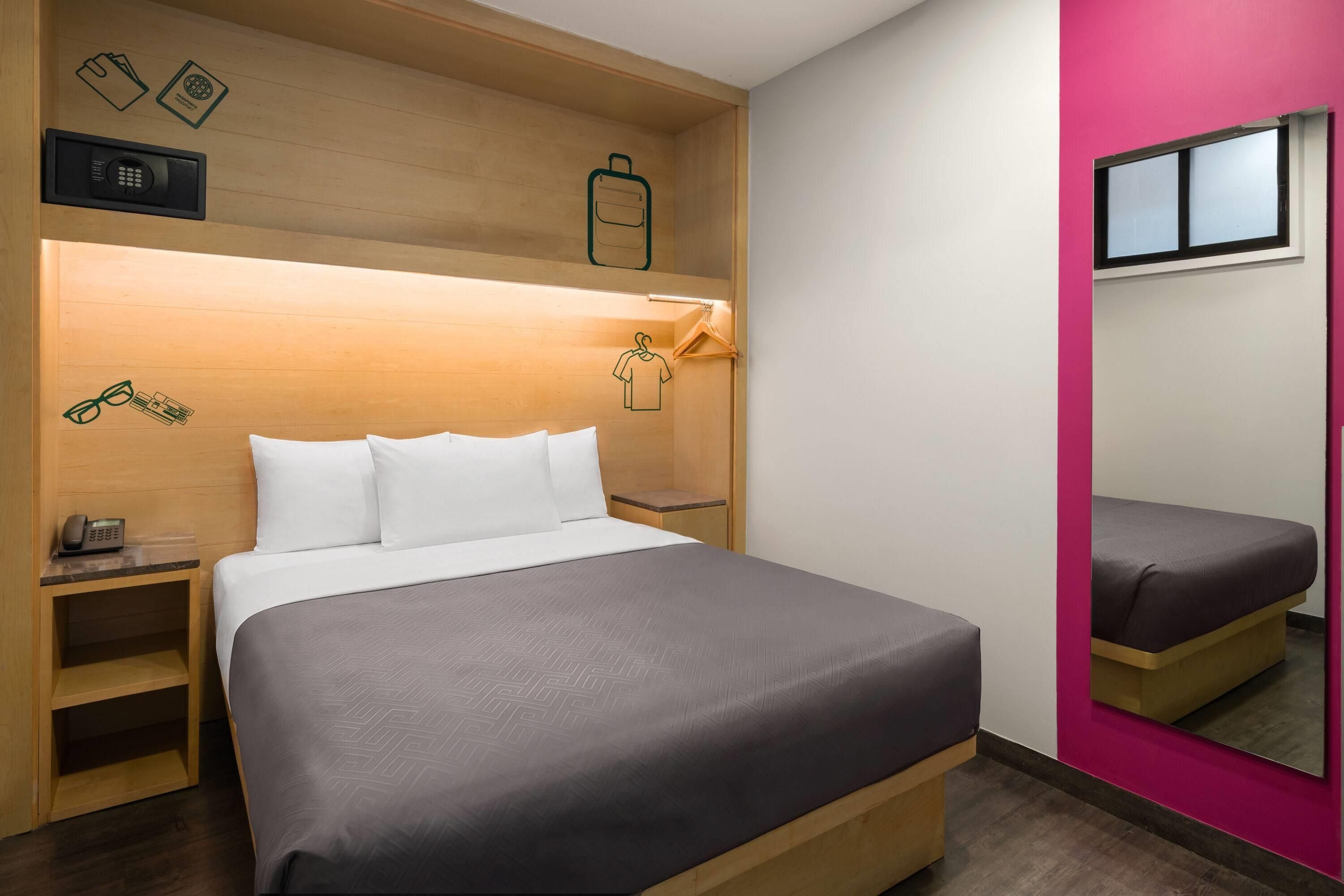 Een hotelkamer met een bed, nachtkastje, spiegel en garderobe.