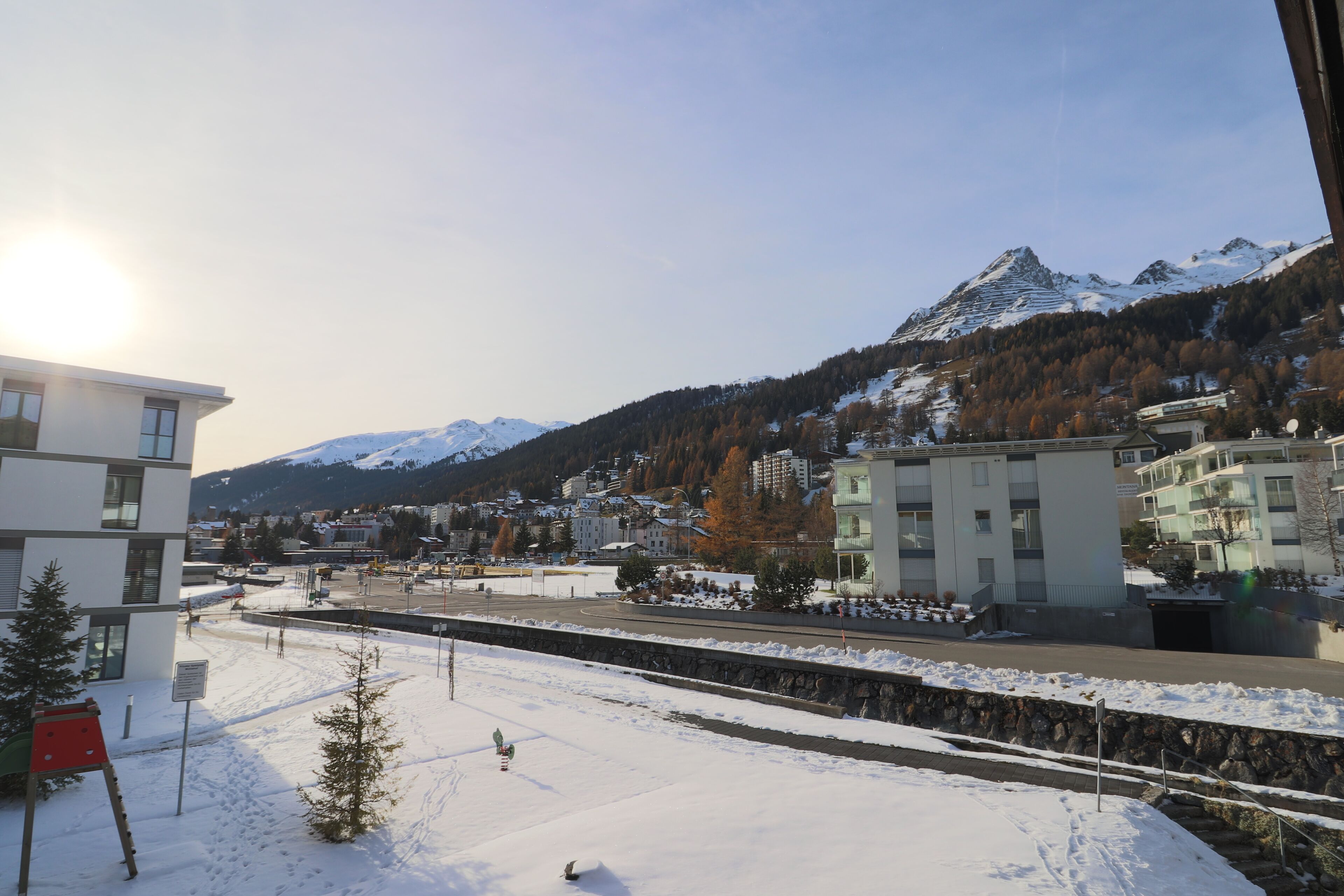 A snow-covered landscape with a mountain in the background, a railway track, and modern buildings.
