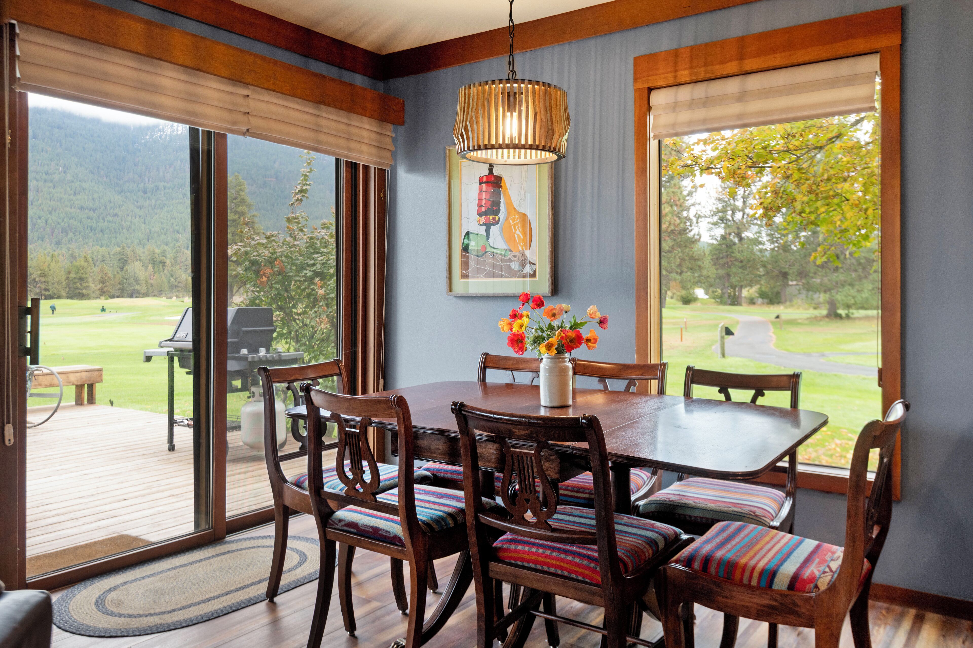 A dining area with a wooden table and chairs, a vase with flowers, and a painting on the wall.