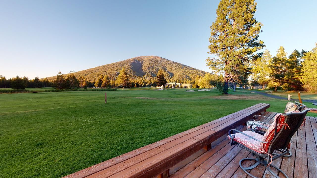 Een houten terras met een bankje en een stoel, uitkijkend op een grasveld met een berg op de achtergrond.