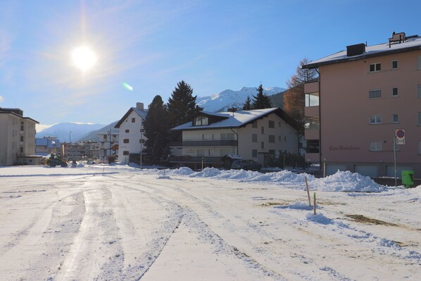 A snow-covered street with buildings, including a pink building with "Casa Monodura" on it. - Apartments Museumstrasse (Davos)