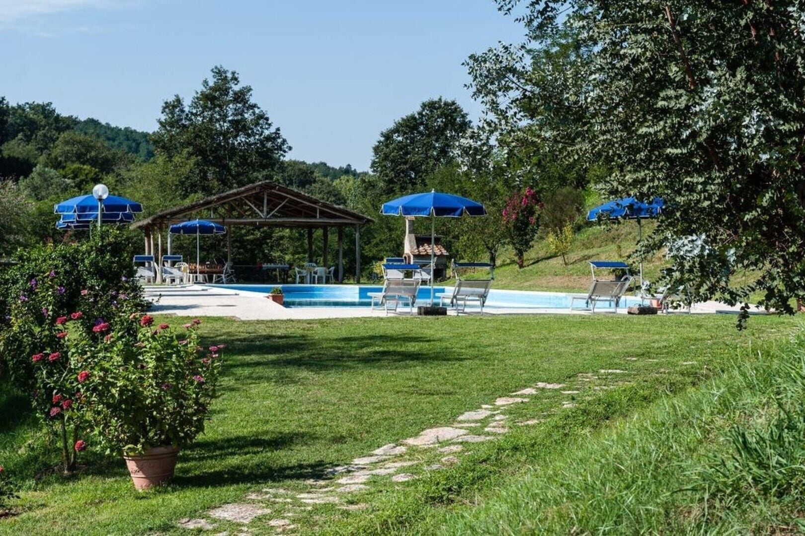 A pool area with lounge chairs and umbrellas, surrounded by greenery and trees.