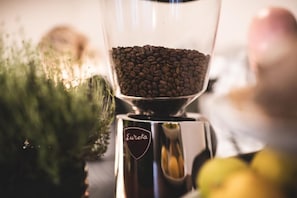 A coffee grinder with coffee beans inside, a green plant, and a bowl of apples.