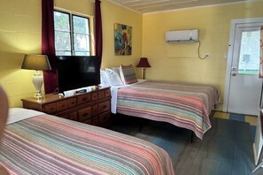 A room with two beds, a television, a painting, and an air conditioning unit.