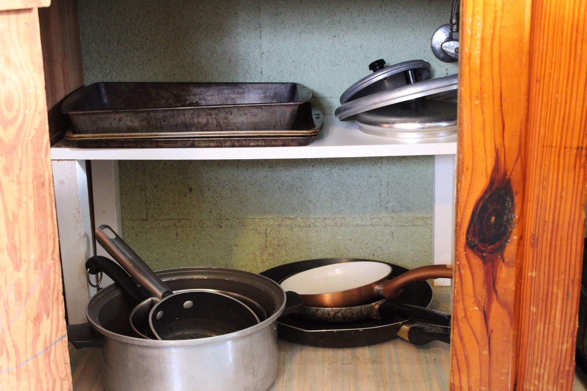 A kitchen shelf with cookware including a frying pan, a pot, and a baking dish.
