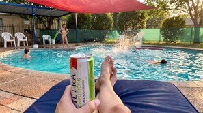 Une personne se détend au bord d’une piscine, une boisson à la main.