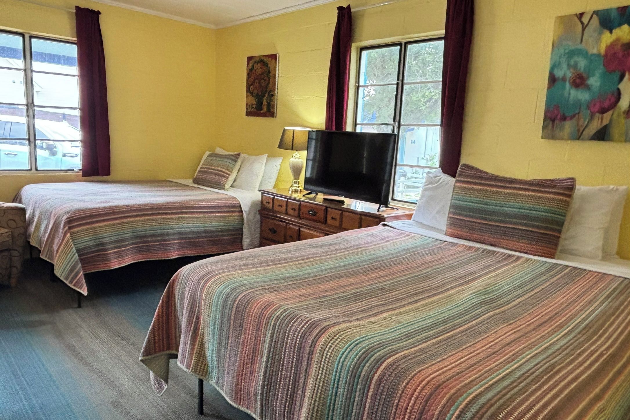 A room with two beds, a television, a dresser, and a painting on the wall.