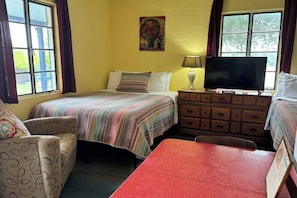 Une chambre avec un lit, une télévision, une commode, une chaise et une table.