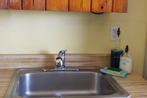 A stainless steel sink with a single faucet, a soap dispenser, and a sponge on a wooden countertop. - Sunfish Studio Cabin 3: Lake LBJ with Pool & Porch! (Kingsland)